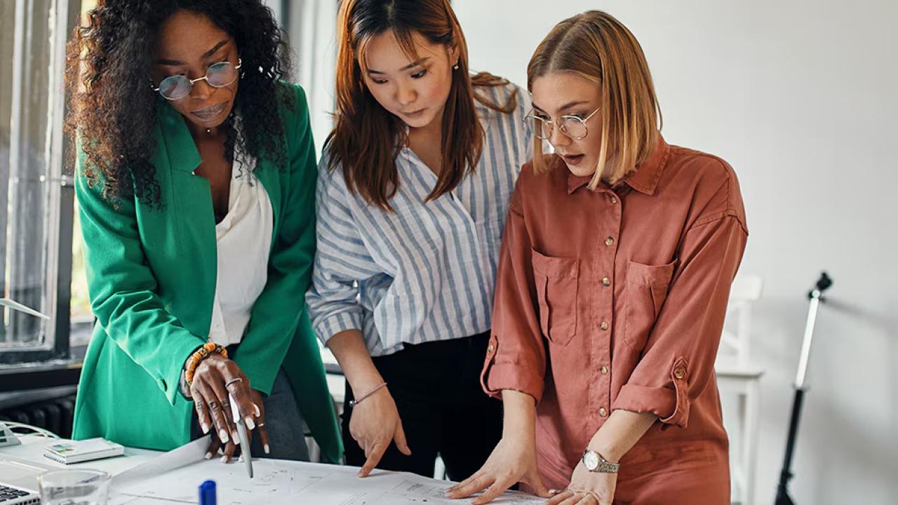 Three women stood at a desk looking at a piece of paper 