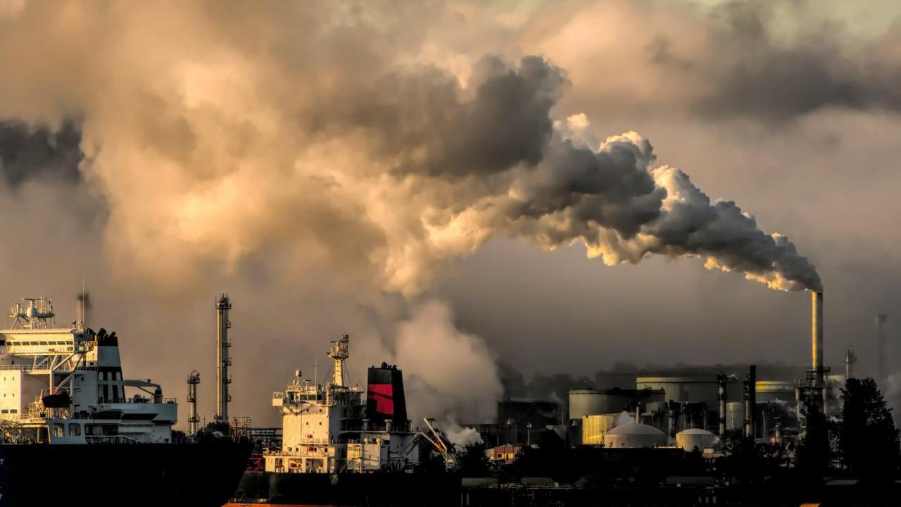 Smoke stacks with billowing clouds and a cloud covered sky behind.
