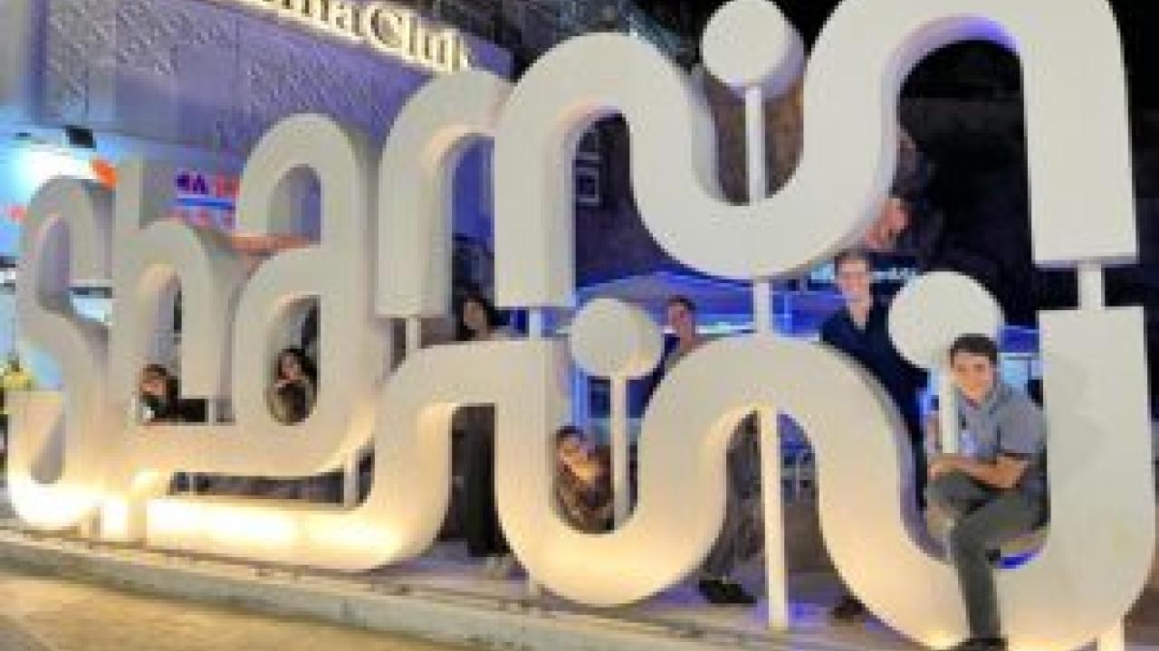 Seven people poking through a large sculpture of letters outside the "Panorama Club".