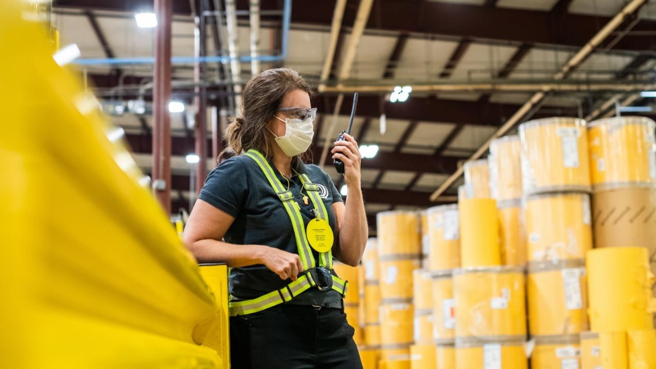Karen Crisp in safety gear standing among yellow barrels in a factory