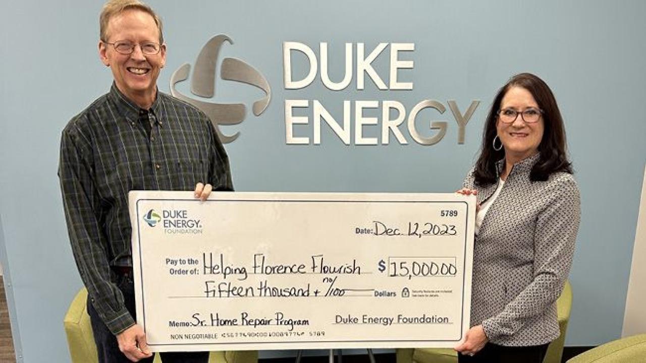 Two people holding a large check. Duke Energy sign on the wall behind them.