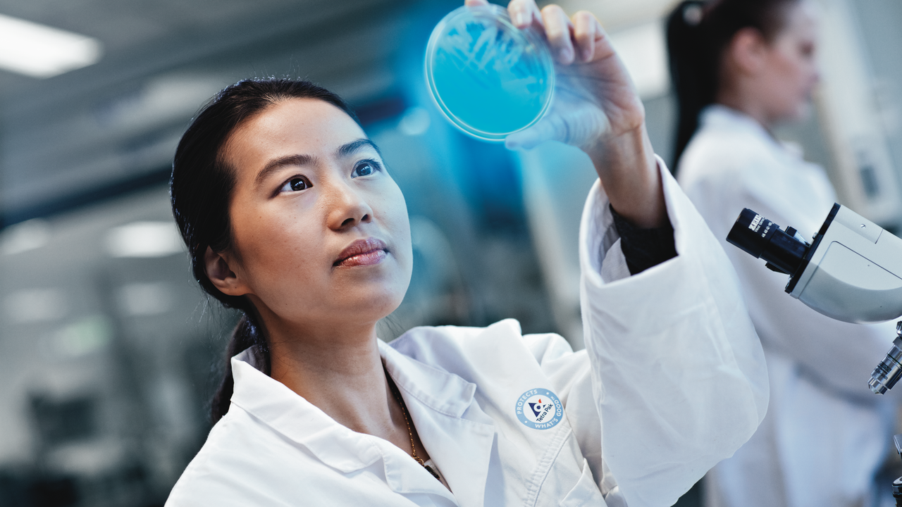 A person in a lab jacket holding up a petri dish that's glowing blue