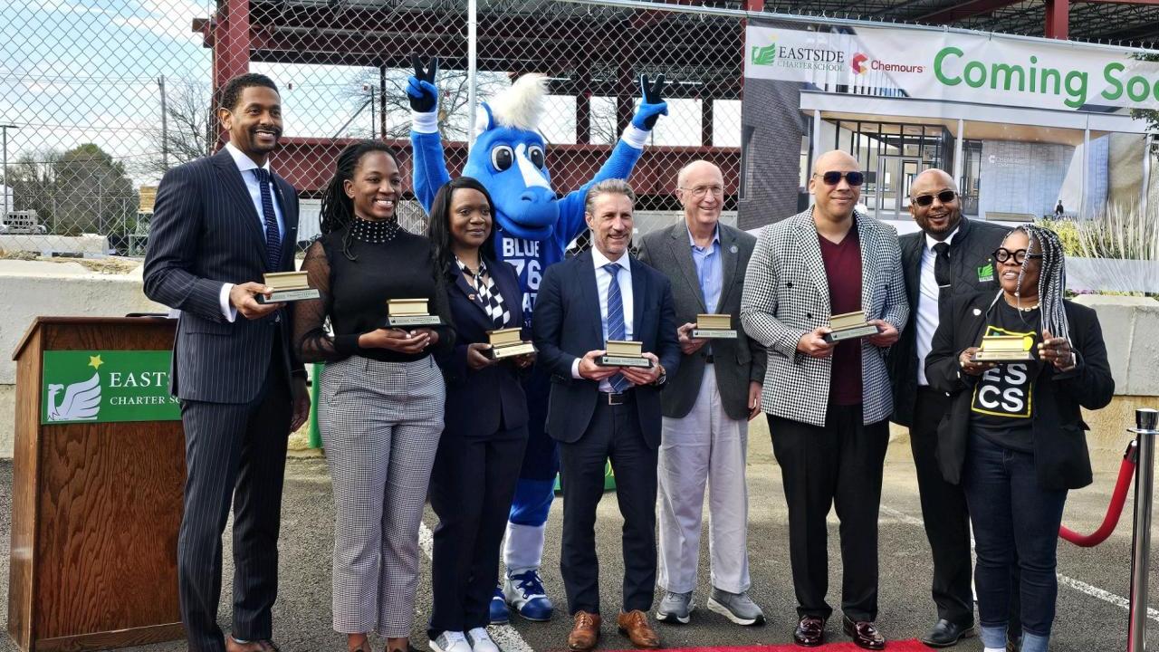 People standing together on a red carpet along with a blue mascot, holding awards