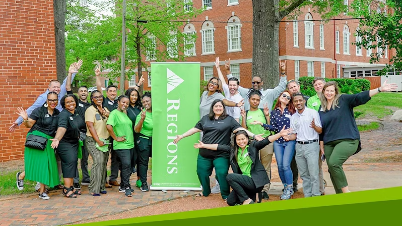 A group of people posing outside next to a Regions banner