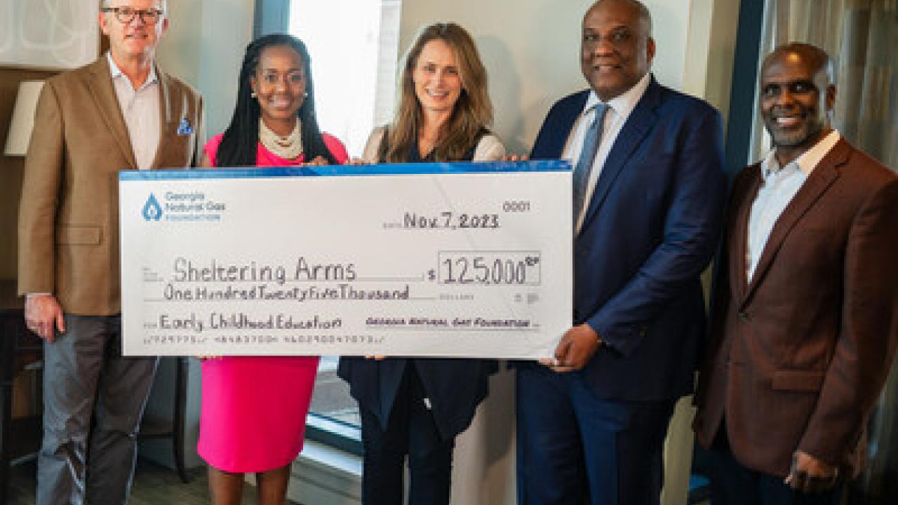 Five people posed with a large check made to Sheltering Arms.