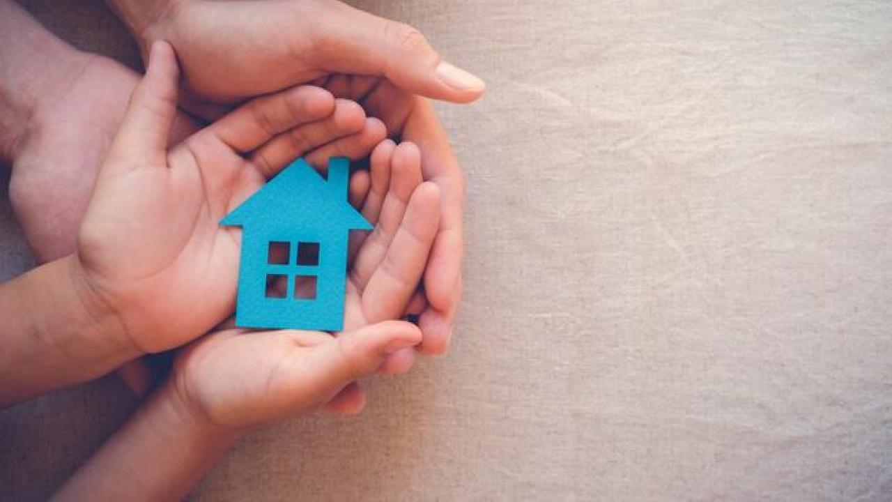 A child resting their hand on top of an adults palm, holding a little blue house figure