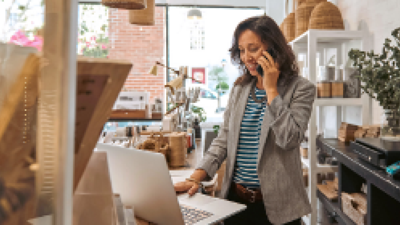 A person in a shop using a phone and working on a laptop