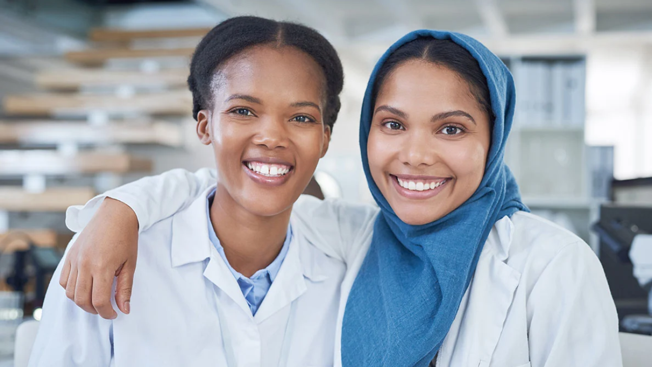 Two women in lab coats smiling