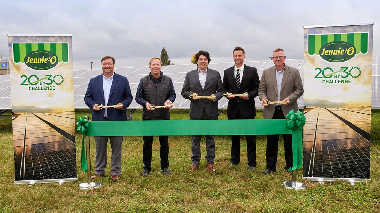 5 executives holding golden scissors behind a green ribbon in front of a solar array