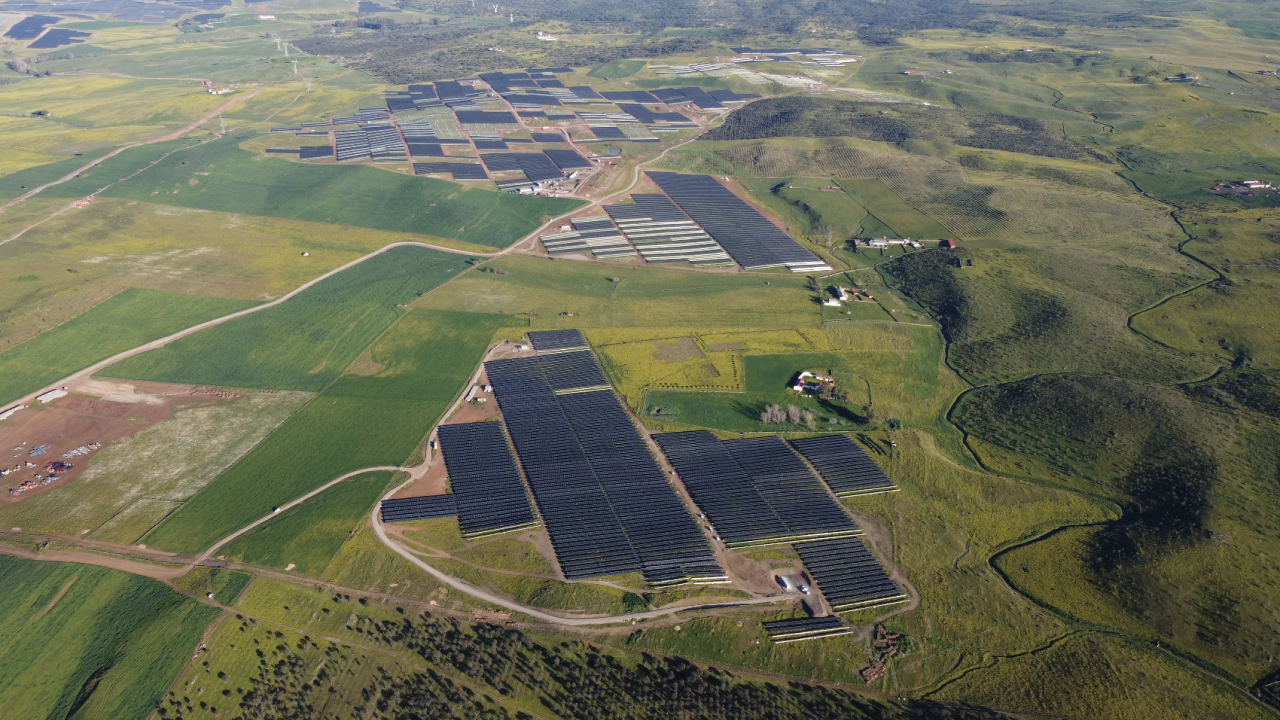 Aerial panoramic view of green fields, solar panels covering parts.