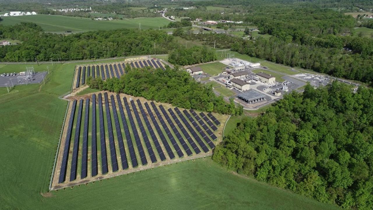 Field of solar panels next to a campus of building in a forested area