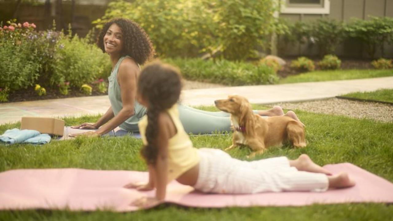 Adult and child doing yoga on a lawn with a dog nearby