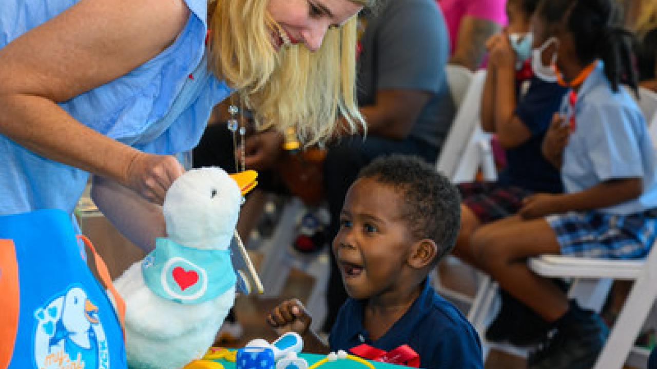a child sitting at a short table, an adult showing them how the robotic, stuffed duck works