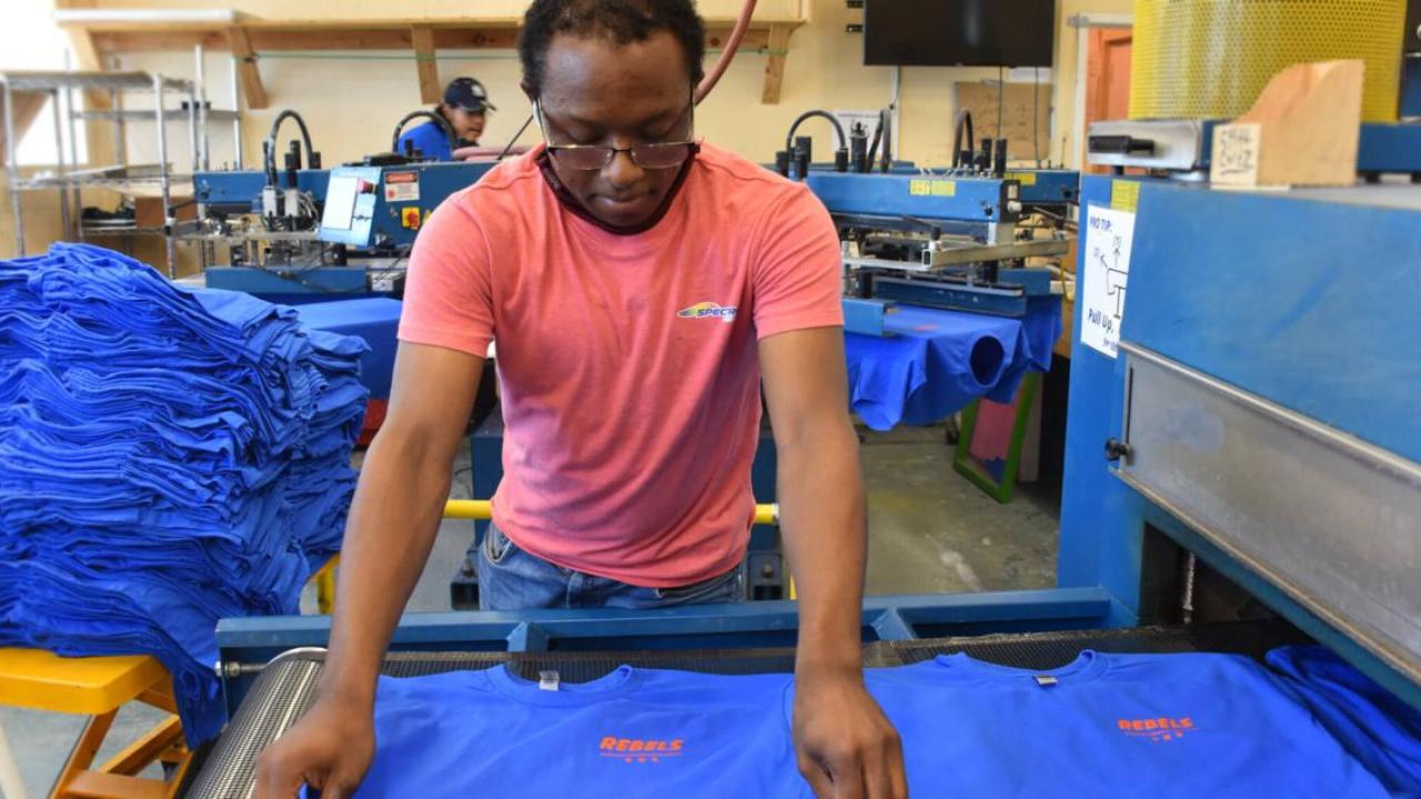 A person lays a t-shirt neatly on a conveyor.