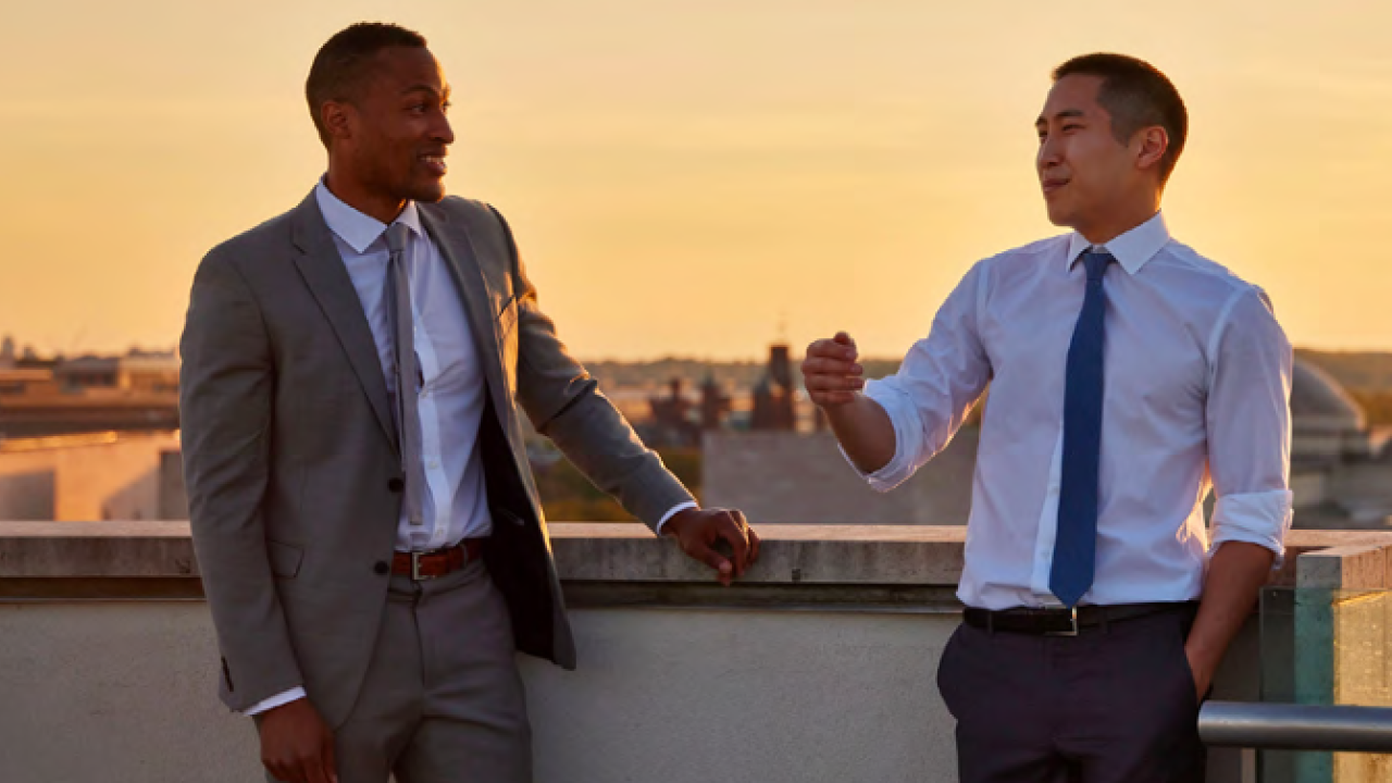 Two people in suits standing on a rooftop talking