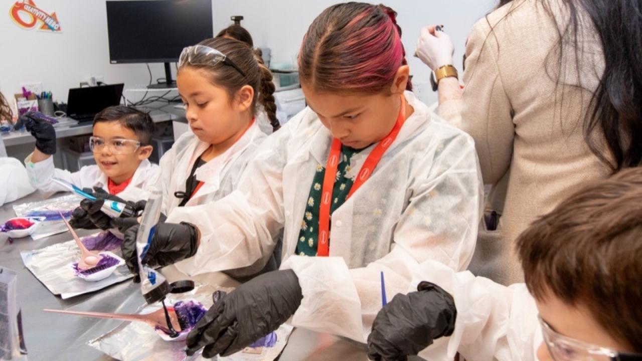 Children in protective lab gear doing experiments at a table.