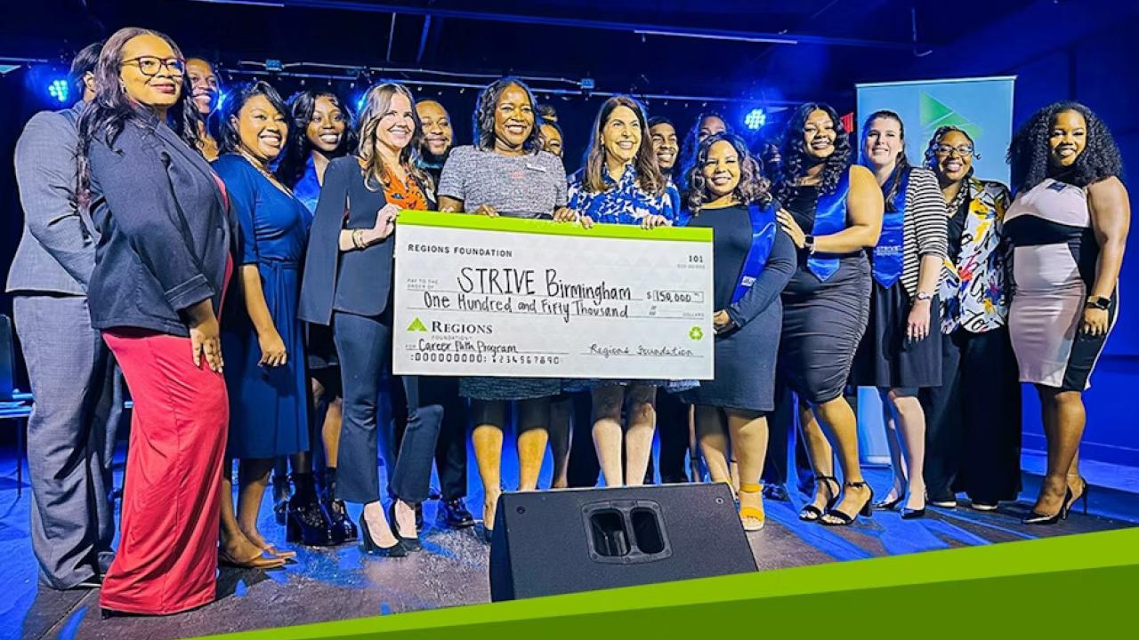 A group posed with a large check on a stage