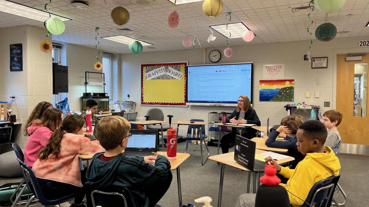 Karen Braun and students at desks in a circle in a classroom.