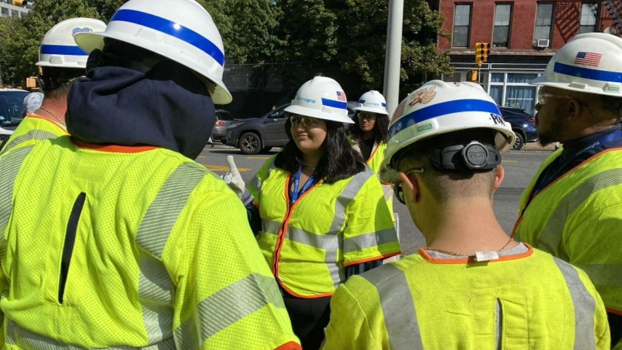 Leela talking to a group of employees. All in high-vis and protective gear outside.