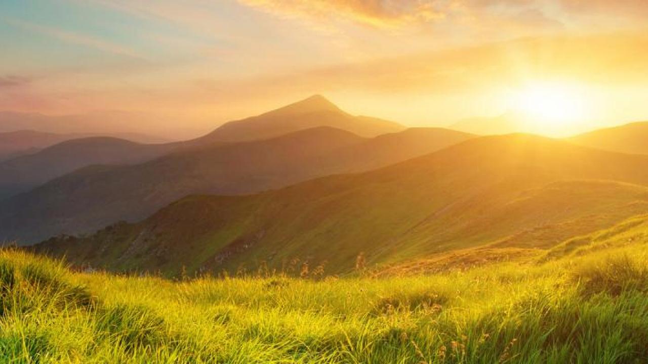 A sunset over mountain range with grassy plains.