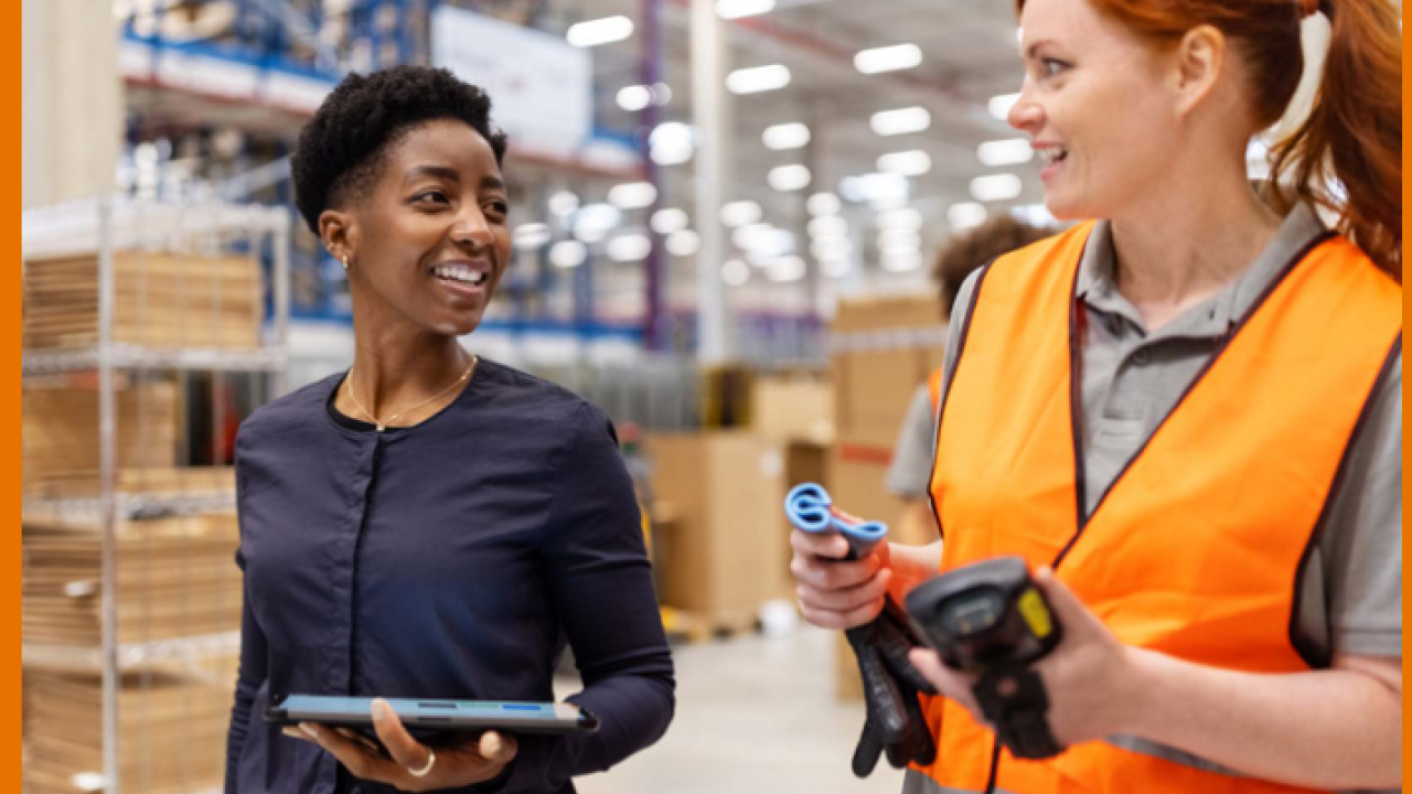 Two people in a warehouse, one wearing an orange vest.