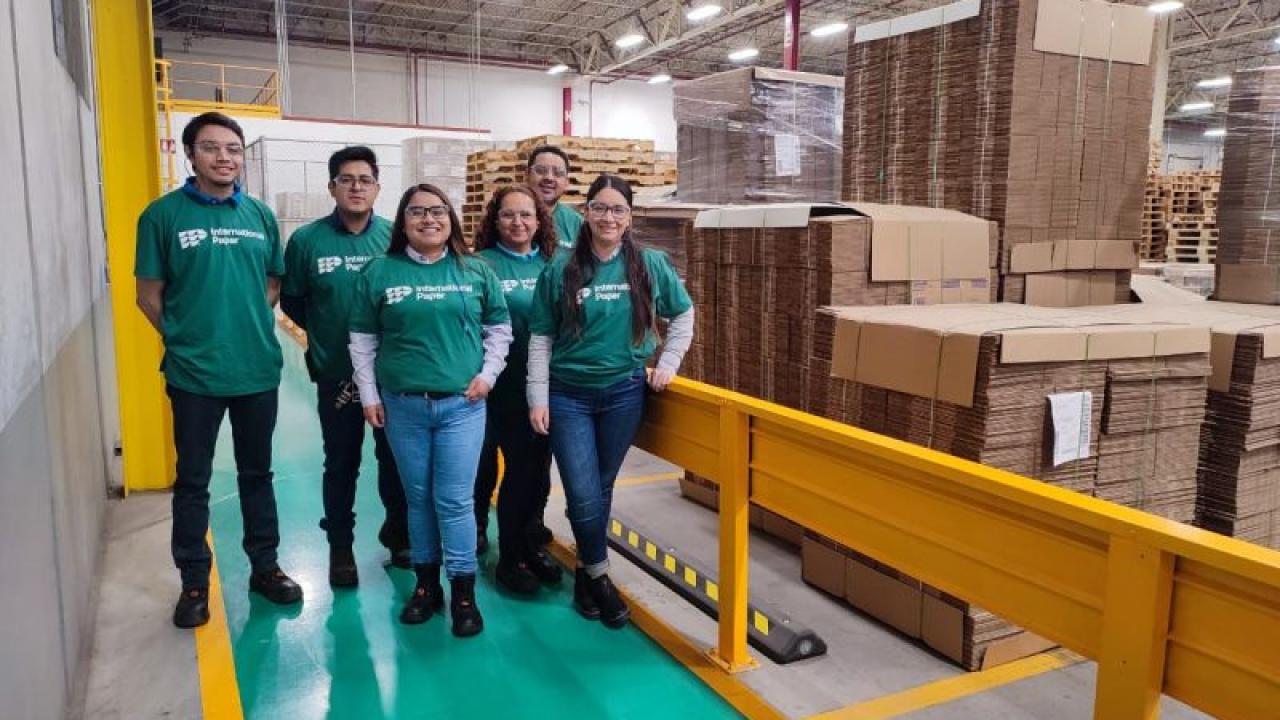 A group of volunteers in matching shirts, a warehouse of paper products behind them.