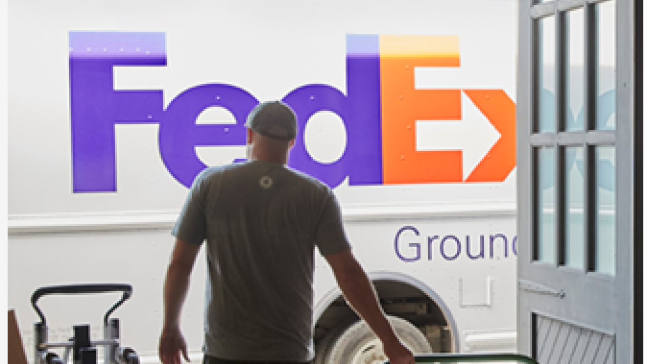 A person pulling a cart wih boxes on it towards a truck with FedEx logo on it.