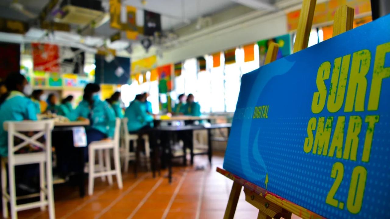 close up of a "Surf Smart 2.0" poster. A group of people seated at tables is blurry in the background