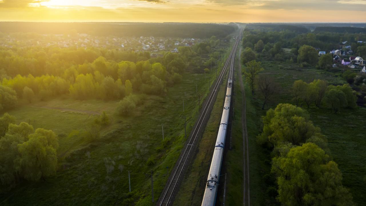 a long train moving through a green landscape at dawn