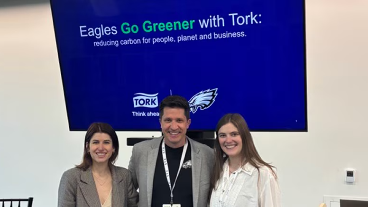 Three people standing in front of presentation. Screen behind says, "Eagles Go Greener with Tork"