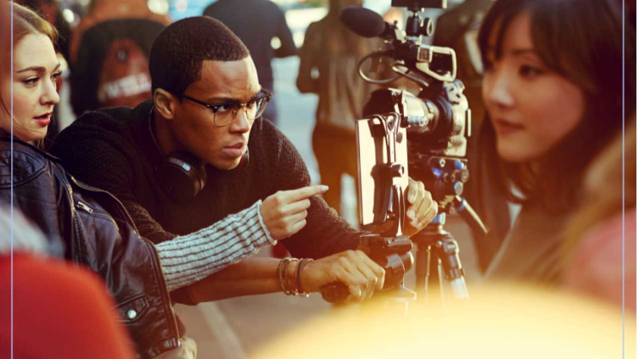 A group of people, some blurred in the background. Some looking at a movie camera