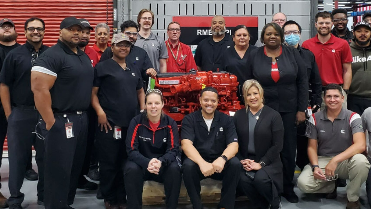 A team posed in a workshop with a large red engine.