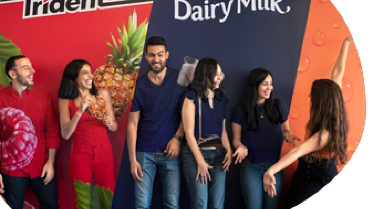 A group of smiling people standing in front of a wall with "Trident" and "Cadbury Dairy Milk" signs.