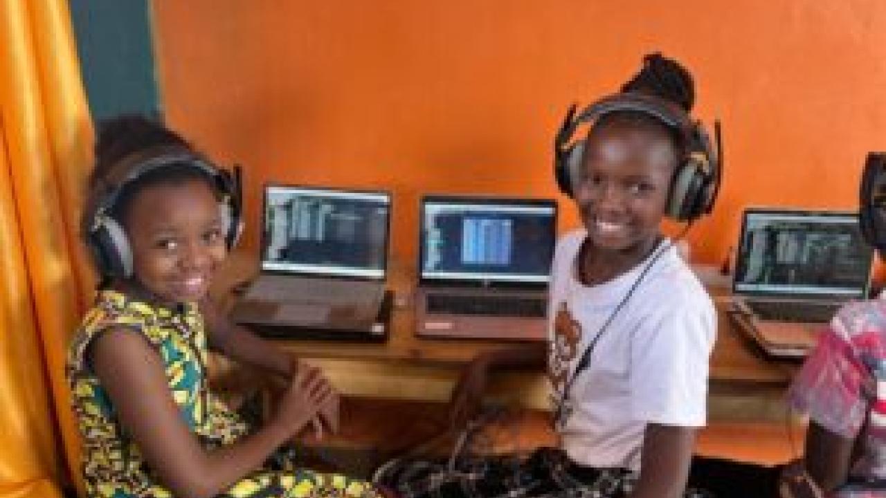 Two smiling children with headphones at a desk with open laptops.