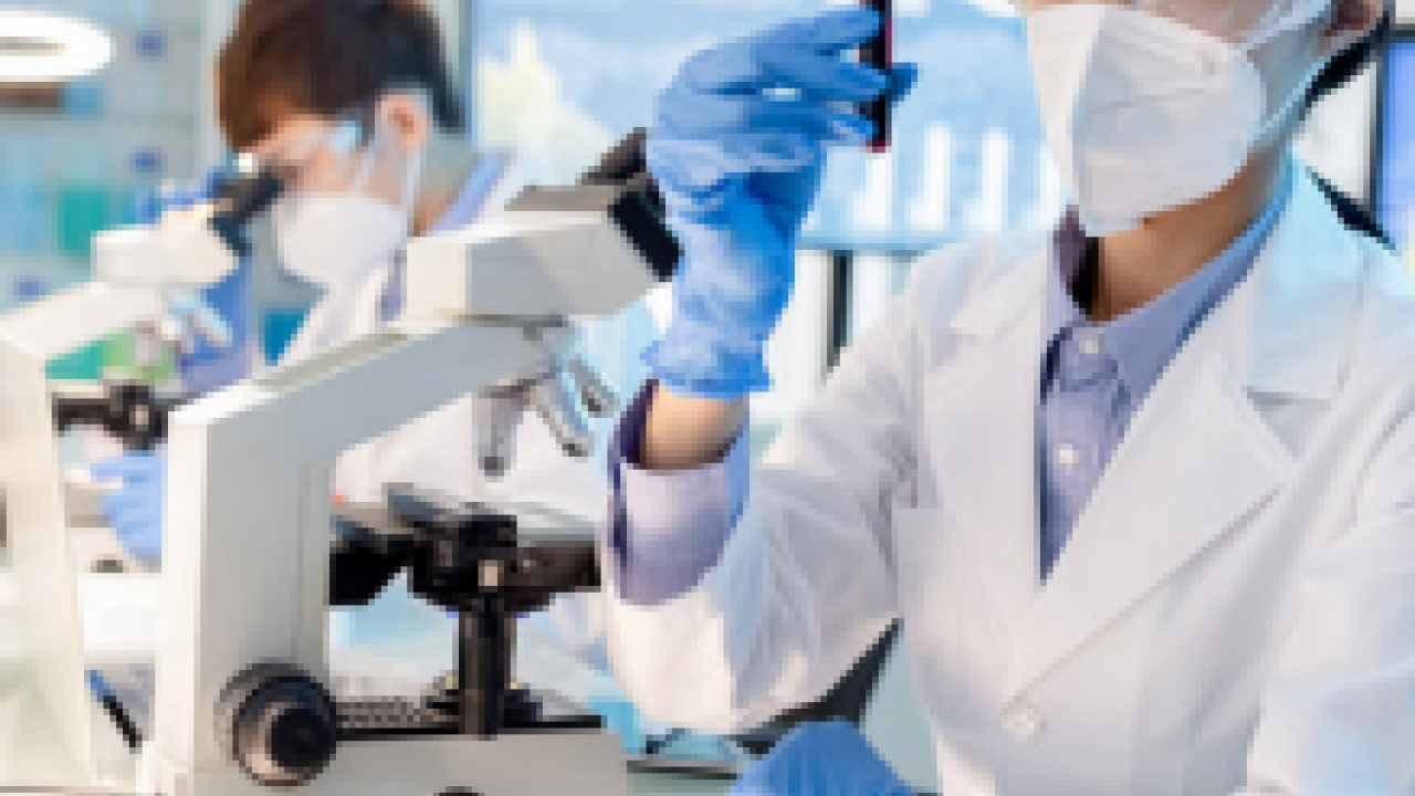 A person holding up a vial of blood next to a microscope