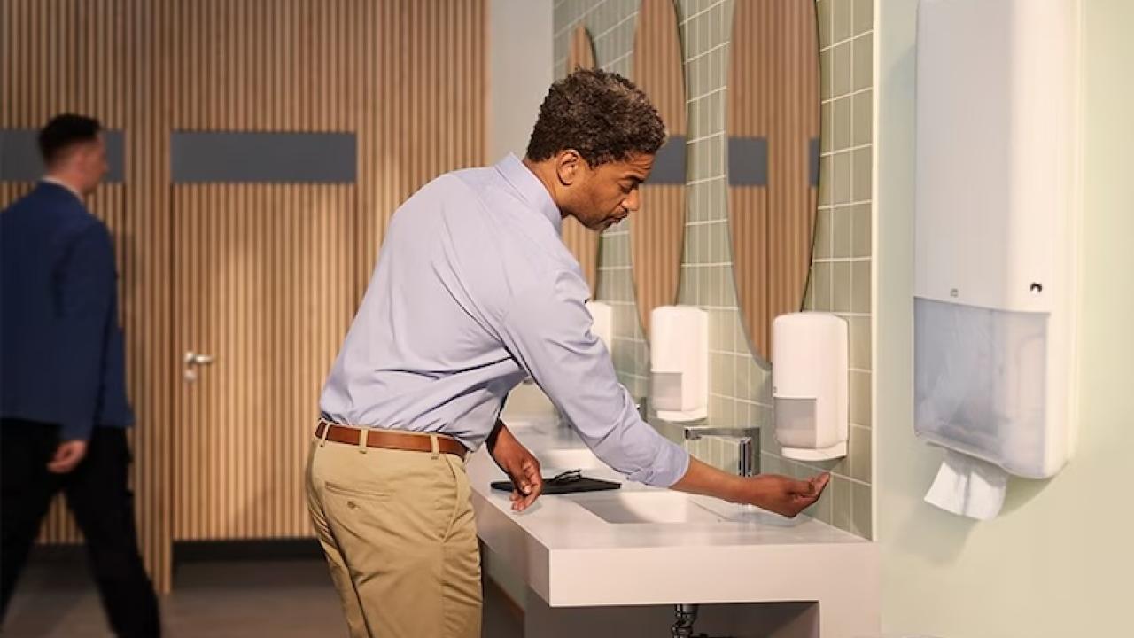 Office worker in a restroom using a soap dispenser.