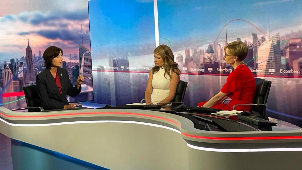 Tracey and two others seated behind a desk on a set.