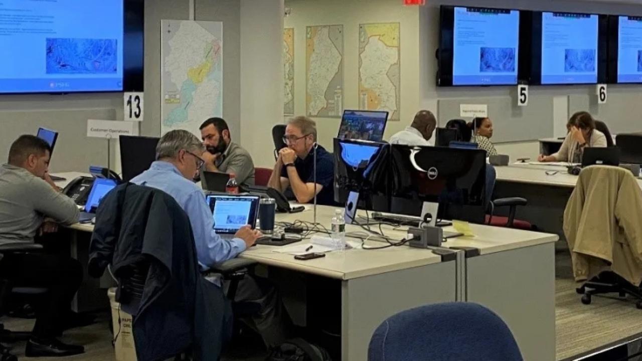 a large room with people seated at stationed tables, many screens on the wall