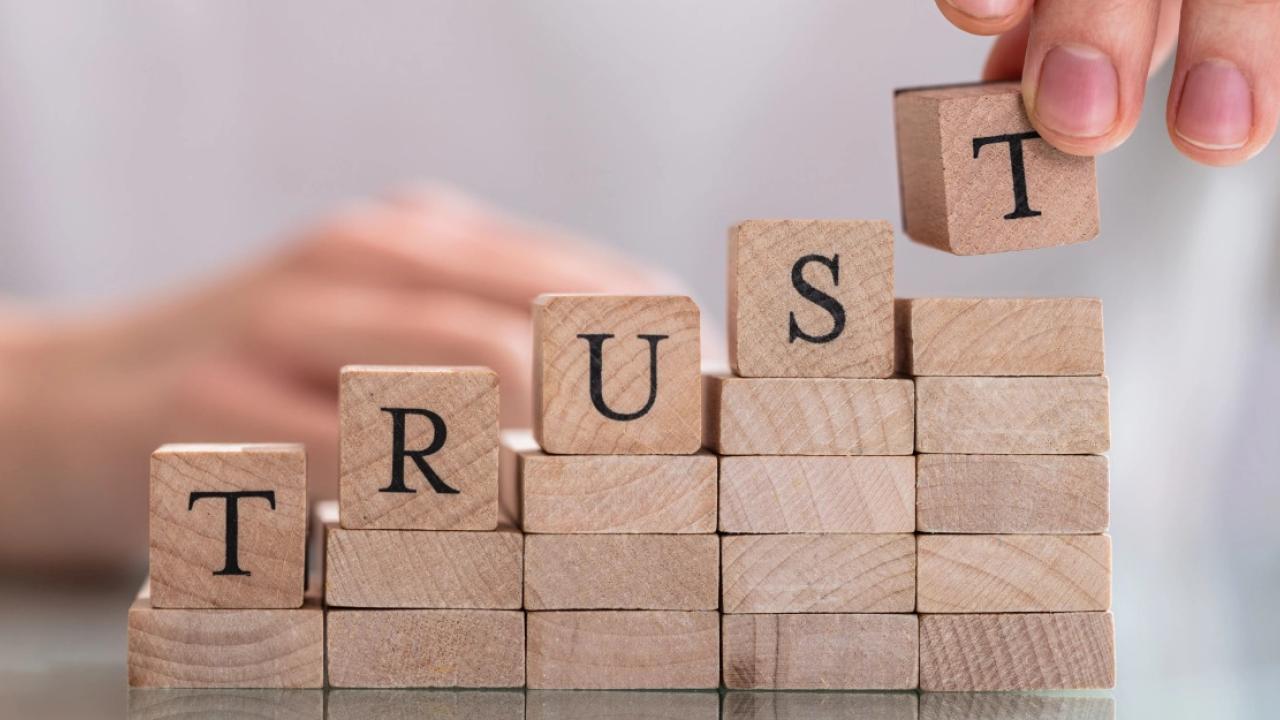 A person stacking wood blocks, the top ones spell out trust.