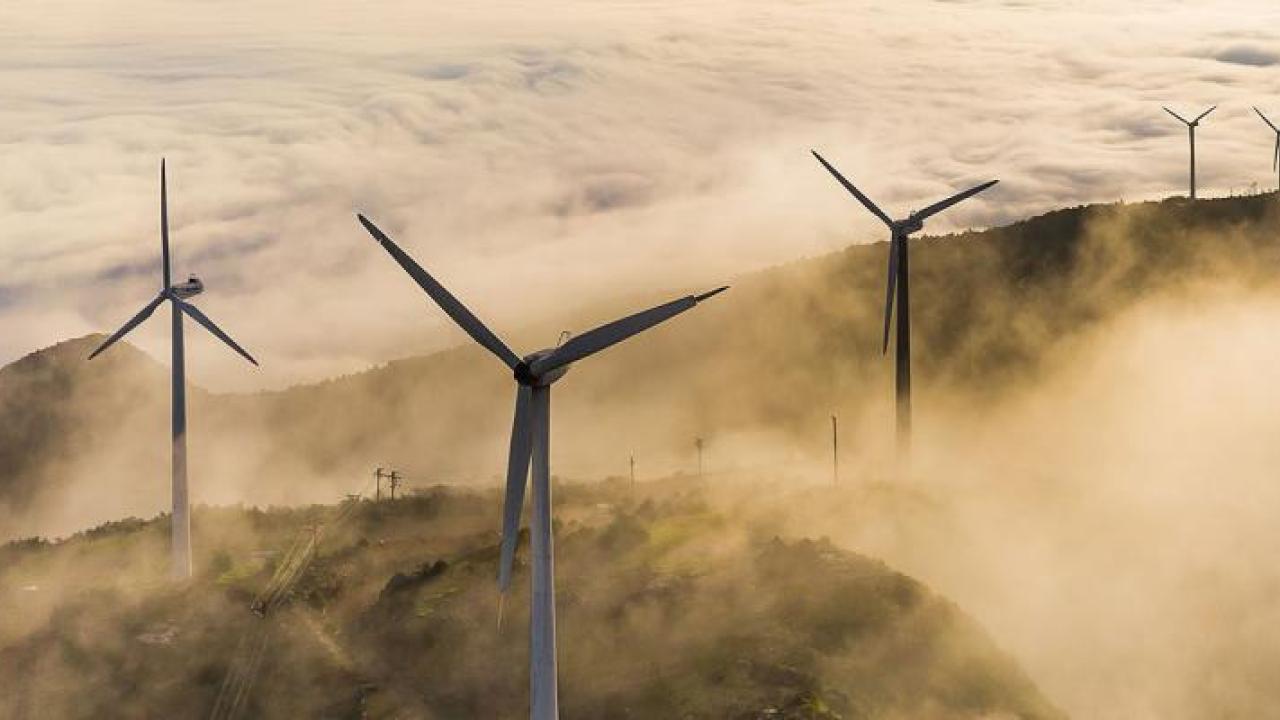 Wind turbines on a high ridge with clouds of fog.