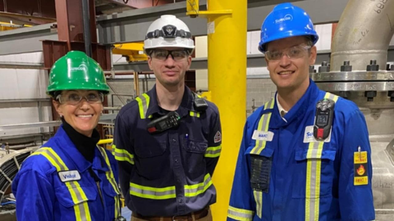 Three people in hard hats, and protective gear standing in an industrial warehouse.