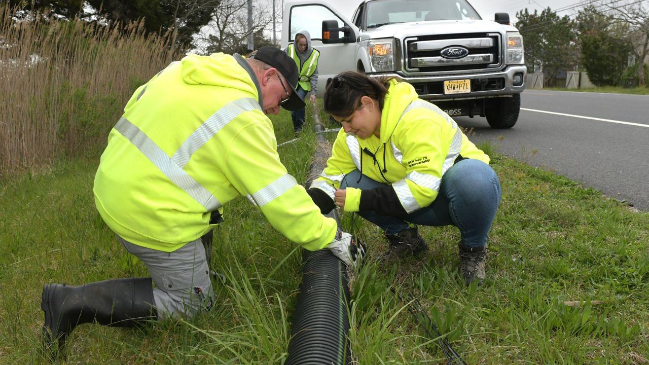 Volunteers working with a drain pipe on the side of a road.