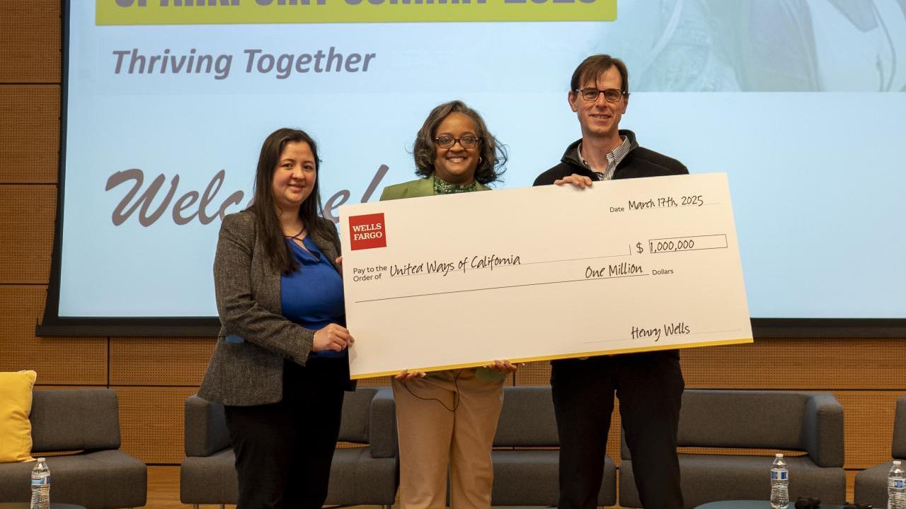 Three people, two women and one man, holding a big check