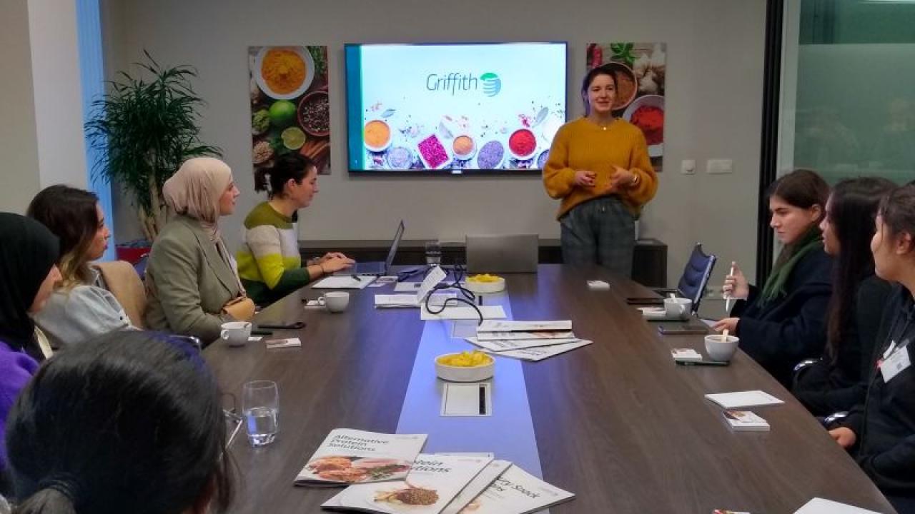 A person presenting to a conference room of others seated.