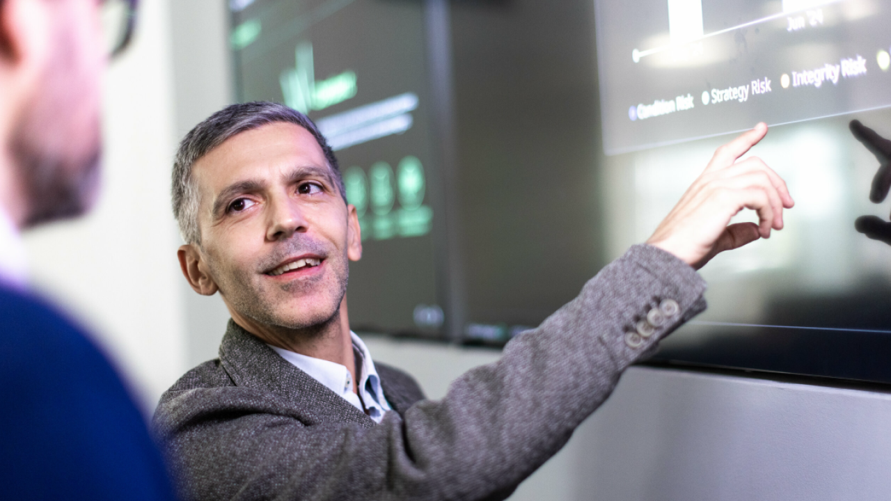 Someone smiling at another person while pointing to a screen