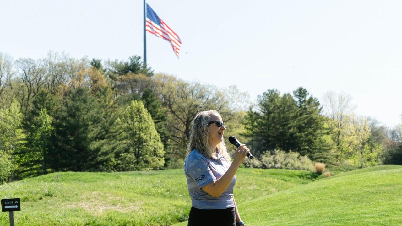 A person standing on a golf course holding a microphone.