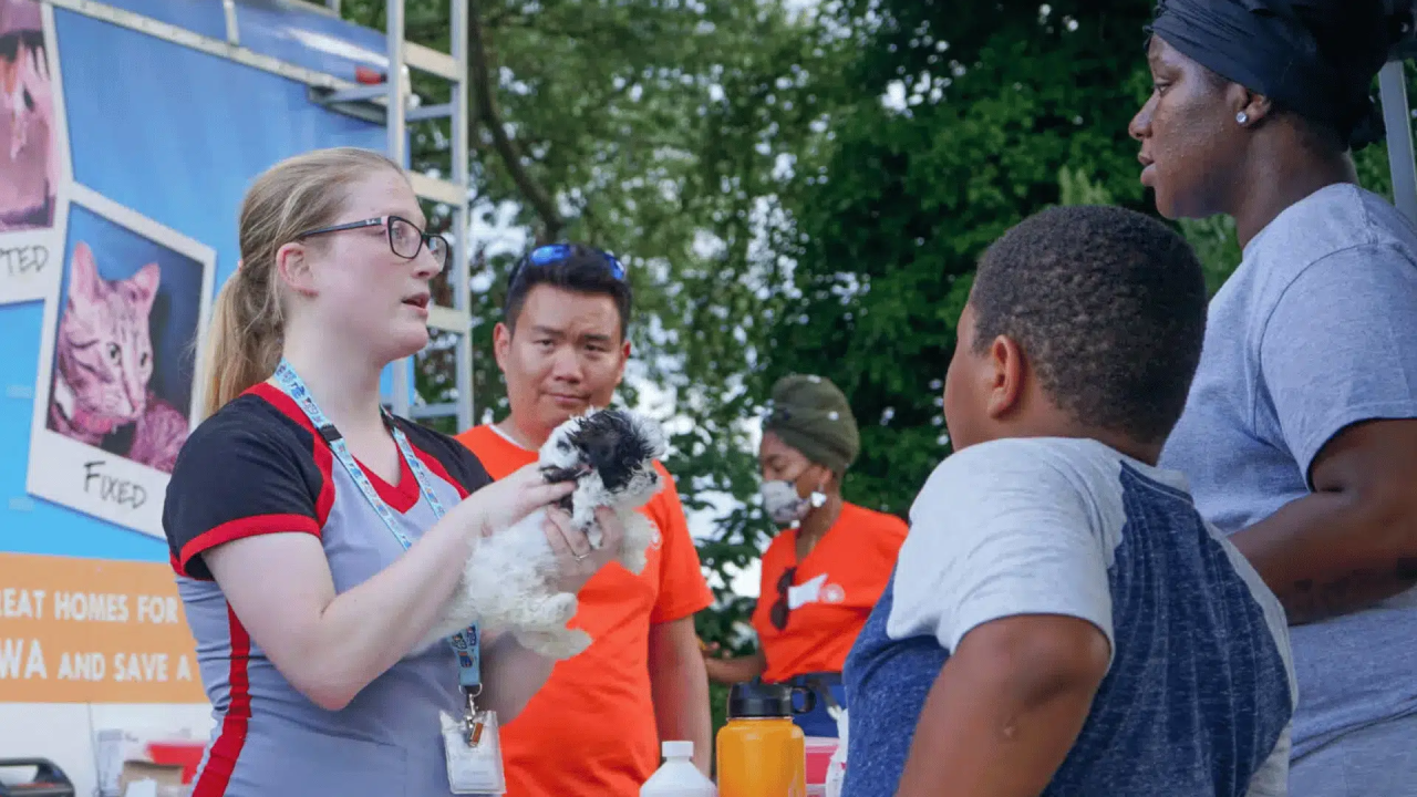 A worker holding a puppy and speaking with people