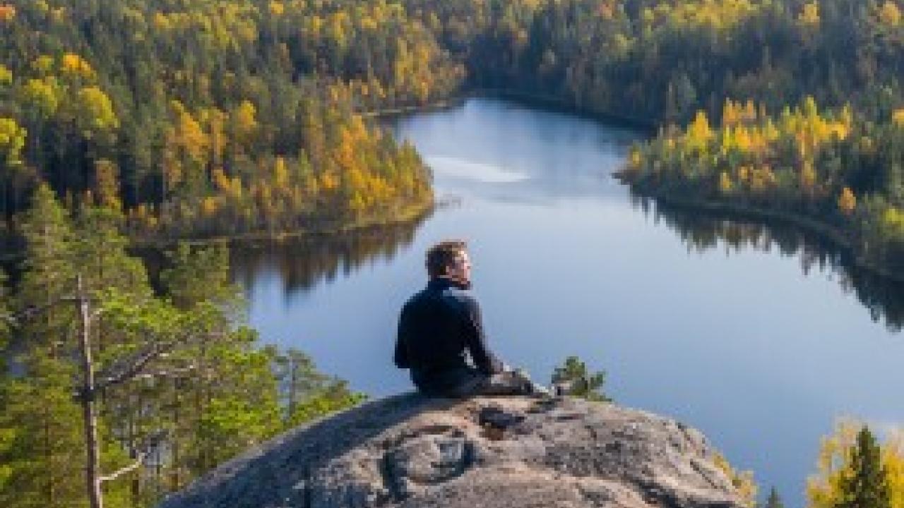 Person sitting on rock, looking over lake