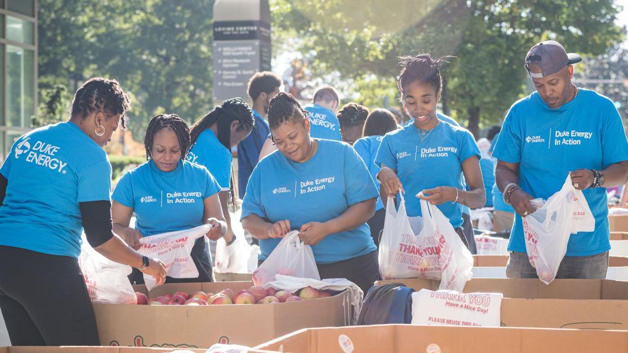 Volunteers packing bags with produce items in large bins outside.