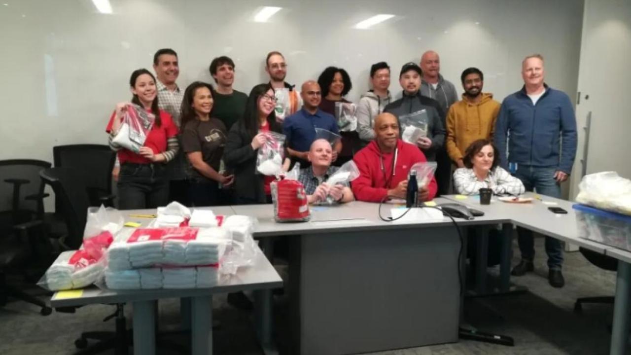 A group posed behind desks, holding bags.